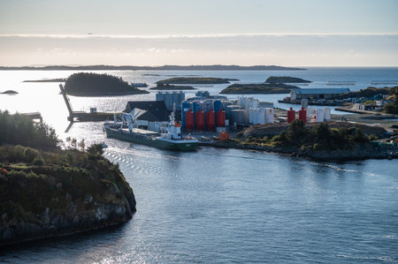 A harbor features a green and white ship docked near industrial storage tanks and surrounded by small islands and calm waters, Haugesund, Norwayの写真素材