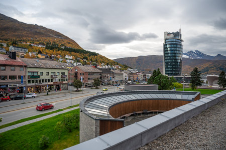 Narvik, Norway, modern building with a curved glass facade stands in a town surrounded by hills and autumn foliage, with a busy street and parked carsの写真素材