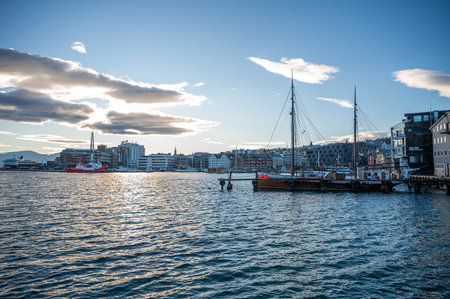 Tromso, Norway. serene harbor scene with a sailboat docked near a city skyline under a partly cloudy skyの写真素材