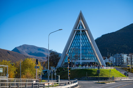 A modern triangular glass building stands prominently in a scenic mountainous area, surrounded by a bustling crowd and a clear blue skyの写真素材