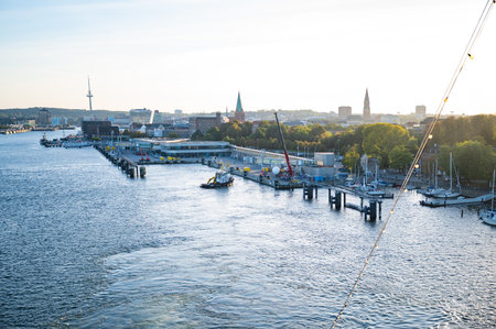 Kiel, serene harbor scene with boats docked, cranes, and a city skyline in the background, with a tower and spiers visible in the distance, Germanyの写真素材
