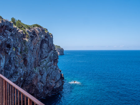 Port de Soller, Mallorca, scenic coastal view with a rocky cliff overlooking the deep blue sea, where a person is swimming near the shoreの写真素材