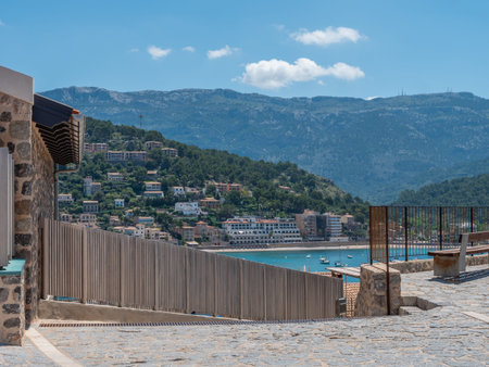 Port de Soller, Mallorca, scenic coastal town nestled among lush hills, with a stone-paved walkway...