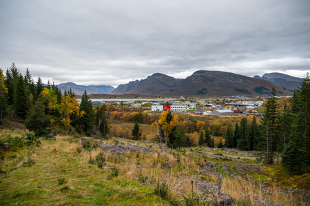 Sortland, Norway landscape featuring the town and industrial area, nestled among autumnal trees, with majestic mountains in the background under a cloudy skyの写真素材