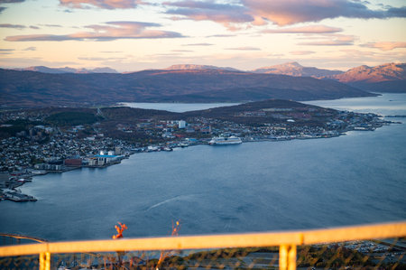 Storsteinen, Tromso, Norway, panoramic view of the coastal city with a harbor, surrounded by rolling hills and distant mountains, bathed in the warm hues of the setting sunの写真素材