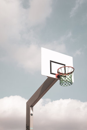 A basketball basket with a green net in front of a blue cloudy sky
