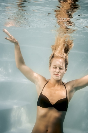 A beautiful blonde woman is diving in the poolの写真素材