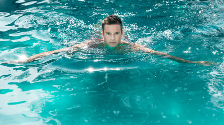 An image of a handsome young man swimming in a pool