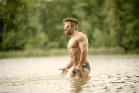 An image of a muscular man in the lake with a white shirt and sunglassesの写真素材