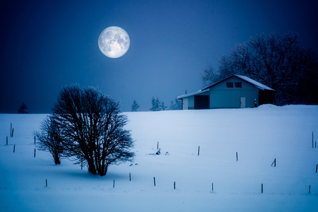 An image of a full moon winter scenery with a houseの写真素材