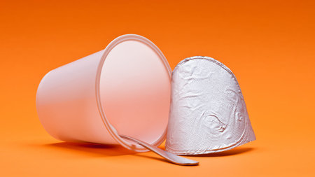 An empty clean yogurt cup with spoon on an orange background