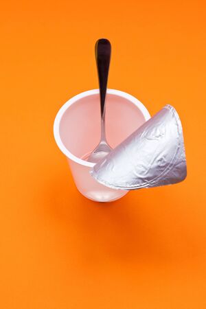 An empty clean yogurt cup with spoon on an orange backgroundの写真素材