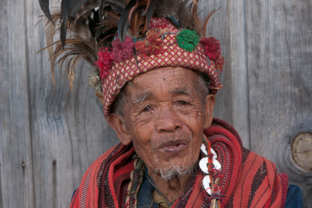 Banaue, Philippines - February 2012: Elder man in traditional clothes sitting in front of a wooden wallのeditorial素材