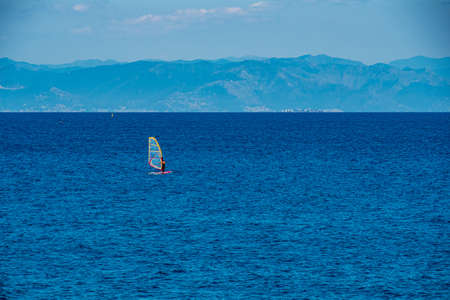 Mediterranean sea with a surfer and an old Italian village in the background - Coast of Bergeggi, Italy, Piedmontの写真素材