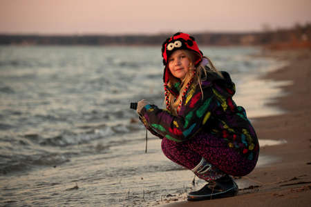 A 9 year old girls takes pictures with a camera at the beach at sunset.の写真素材