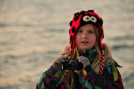 A 9 year old girls takes pictures with a camera at the beach at sunset.の写真素材