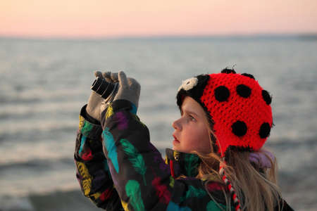 A 9 year old girls takes pictures with a camera at the beach at sunset.の写真素材