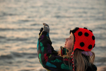 A 9 year old girls takes pictures with a camera at the beach at sunset.の写真素材