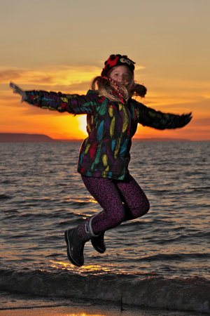 A young girl jumps for joy in front of the setting sun at the beachの写真素材