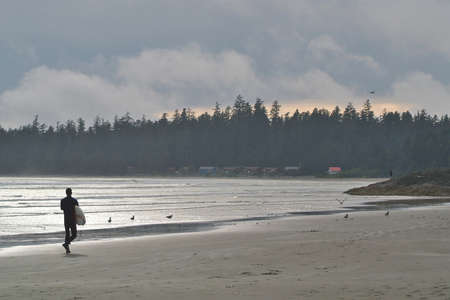 A Surfer Carries his Board Along the Beach in Tofino British Columbia in Canadaの写真素材