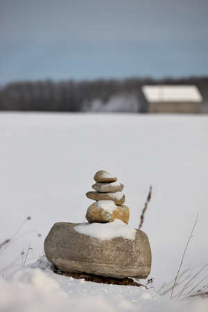 An Inukshuk in a field in the winter with a barn in the distant background. High quality photoの写真素材