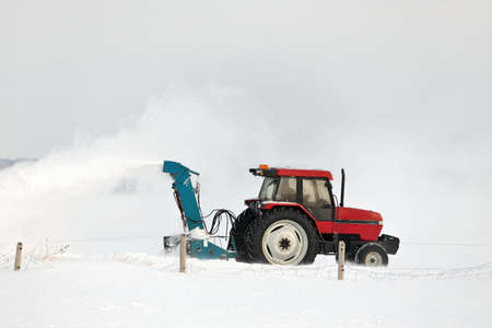 Red Tractor Snow Blowing a Driveway in a Rural Settingの写真素材