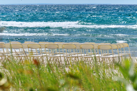 White Folding Chairs Arranged in Rows for a Wedding at a White Sandy Beach on a Sunny Summer Dayの写真素材