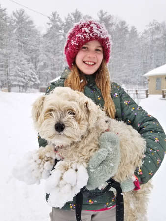 Portrait of A Smiling young girl holding up her Extremely Shaggy Dog Whose Paws are Caked in Snowの写真素材