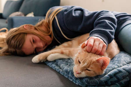 An Young Adolescent girl lying on a couch finds comfort by snuggling close to and petting her catの写真素材