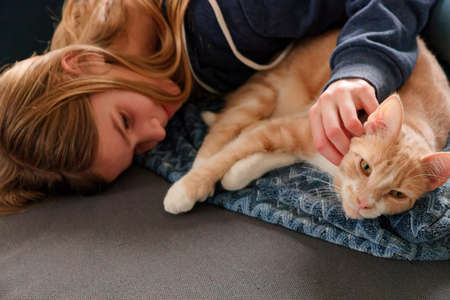 An Young Adolescent girl lying on a couch finds comfort by snuggling close to and petting her catの写真素材