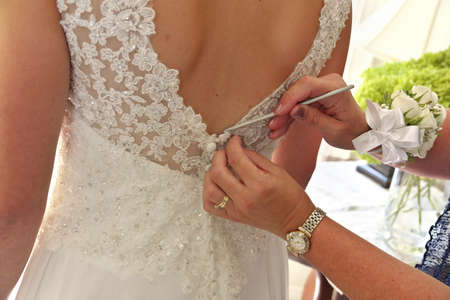 Close up of Hands Doing Final Buttoning of Brides Wedding Dressの写真素材