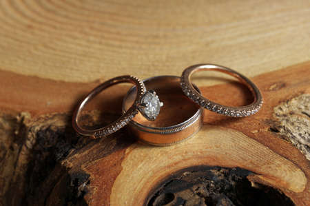 White Gold and Diamond Wedding and Engagement Rings Arranged on Rustic Wood Tree Sliceの写真素材