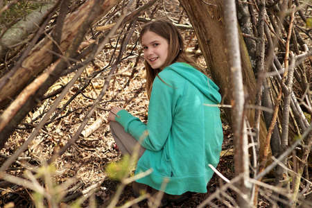 Young adolescent girl outside in the forest with lean-to tree fort treehouse tree house she builtの写真素材