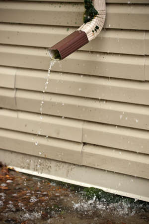 Rain Water Pours Out of a Short Downspout on side of house pooling by foundationの写真素材