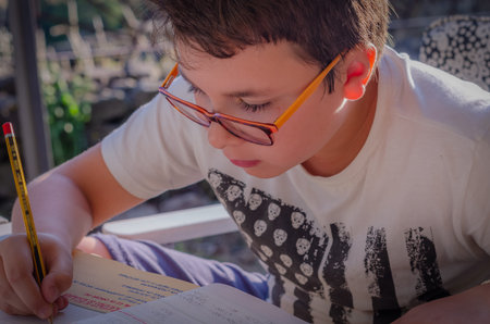White boy with glasses writing with pencil the exercises of the school