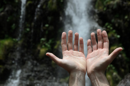 Hands raised towards a waterfallの写真素材