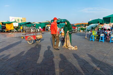 Couple of man and woman talk surrounded by shadows in the square of Plaza de Yamaa el Fna in Marrakech in October 2019のeditorial素材