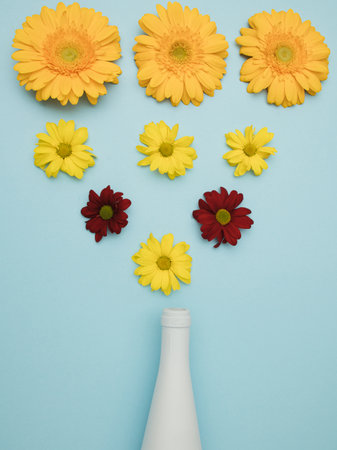 white bottle on baby blue background with fresh flowers and green leaves. Minimal flat layの写真素材