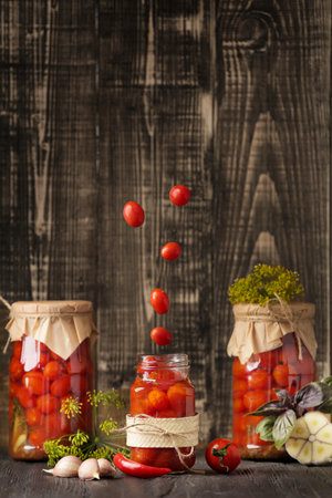 Canned homemade tomatoes. Tomatoes fall into a jar on a wooden background with space for text. An open jar with cherry tomatoes flying into it. Tomatoes fall into a jarの写真素材