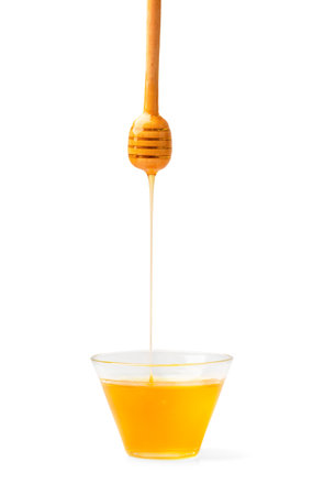 Honey in a bowl with honey flowing from a spoon on a white background. Honey with honey dipper isolated.の写真素材