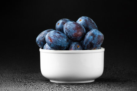 Blue plum in a white plate with water drops on a dark background. Useful dietary fruit.の写真素材