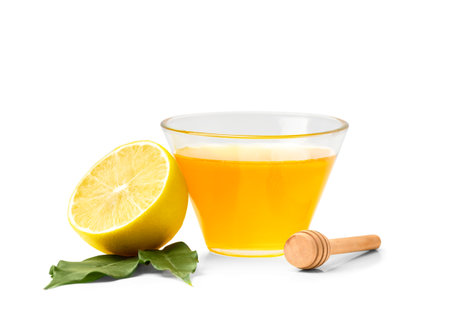 Honey in a glass jar and lemon with leaves on a white background. Closed jar with honey and honey stick on isolationの写真素材