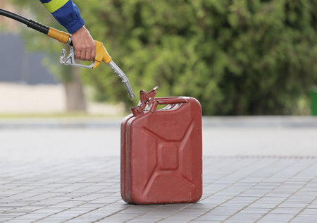 A man fills jerry cans at a gas station. A man fills gasoline in a canister at a gas station. Pouring gasoline into a canister. Collecting funds to buy fuel.の写真素材