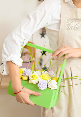Girl makes flowers from the soap. Hobby, creative process. DIY gifts. Women's hands and flowers. handmade soap. Mother's Day, Women's Day. natural organic products. Flowers on a white table. Roses in a green basket.の写真素材