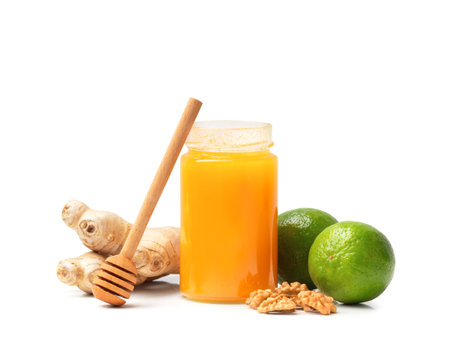 Honey in an open jar with nuts, lime and ginger on a white background. Healthy foods. Honey in a glass jar with honey stick on isolationの写真素材