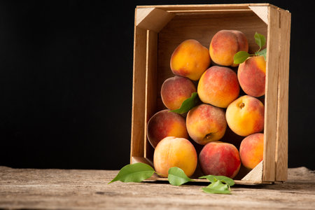 Peaches in a box on a wooden background top view. Fresh fruits on a vintage background. Peaches on a wooden background. Summer fruits in a wooden box. Peaches on a black background.の写真素材