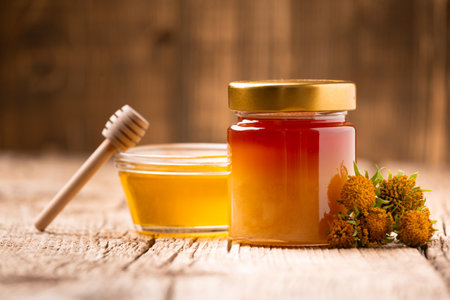 Honey in a closed glass jar and a bowl on a wooden background. Composition of honey jars, dipper and flowers. Healthy foods. organic honey. organic products.の写真素材