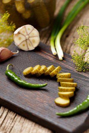 Sliced pickled cucumber on a dark wooden board. Cucumbers in a jar, cucumber slices, chili peppers, garlic, green onions on a wooden background. Still life of vegetables and spices on a dark background.の写真素材