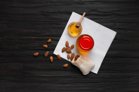 Honey is poured from a dipper into a glass bowl and almonds poured out of a bag on a wooden background top view. Still life of honey and scattered nuts on an aged wooden background.の写真素材