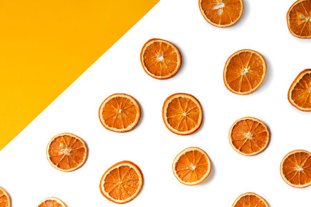 Dry slices of orange are laid out on a white and yellow background top view. Orange chips on...